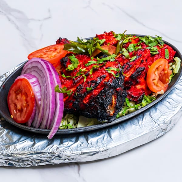 Dasara Indian Cuisine's Tandoori Chicken, garnished with cilantro, red onions, and tomatoes, served on a hot plate.