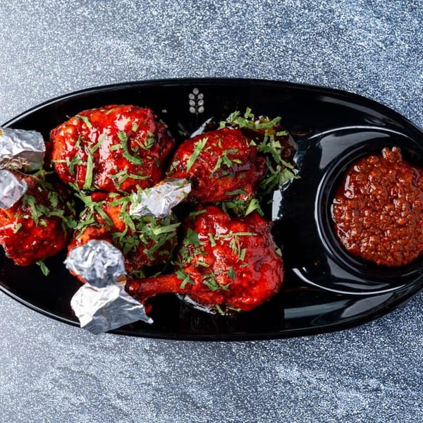Dasara Indian Cuisine's Chicken Lollipops, glazed red with herbs, served on a black platter with dipping sauce.